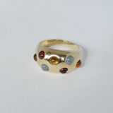 A gold-colored wide band ring with multiple multicolored gemstone accents.