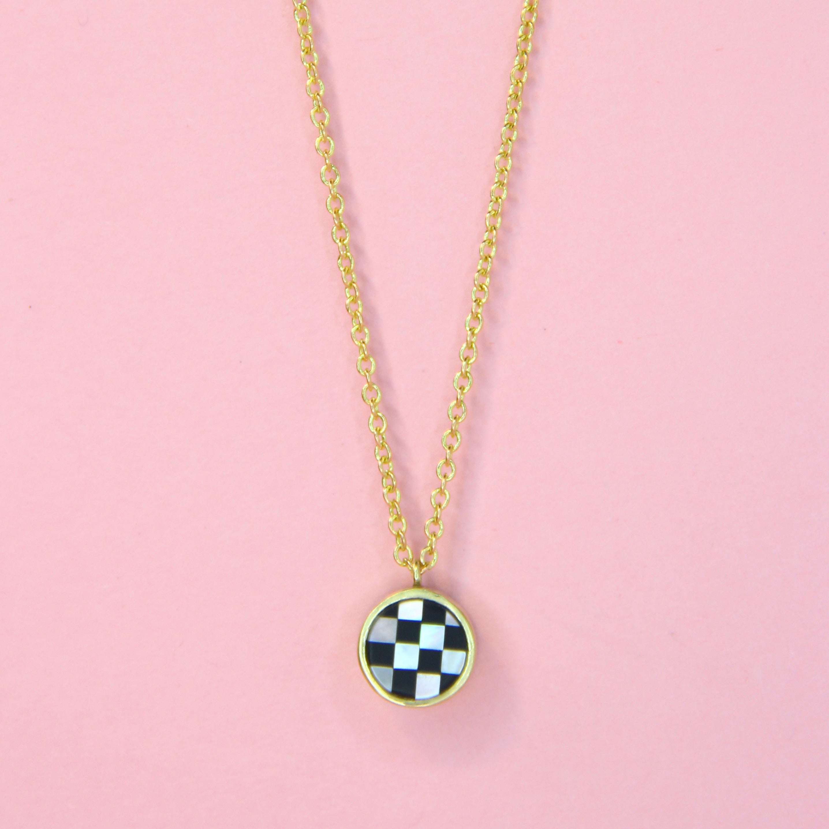 A gold toned necklace on a delicate chain with checkerboard inlay with mother of pearl and glass
