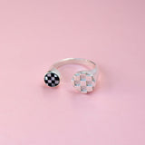 A silver split shank ring with a silver metal checkerboard pattern on on side and a mother of pearl and black glass inlay pattern on the other