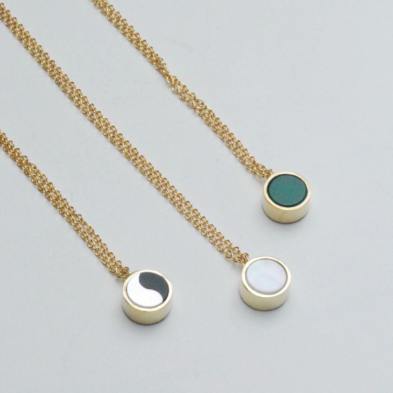 Three gold toned necklaces with chrysoprase, mother of pearl, and ying yang shown on a white background