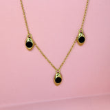 Bronze gold toned necklace with three black onyx inlaid stone charms on a pink background
