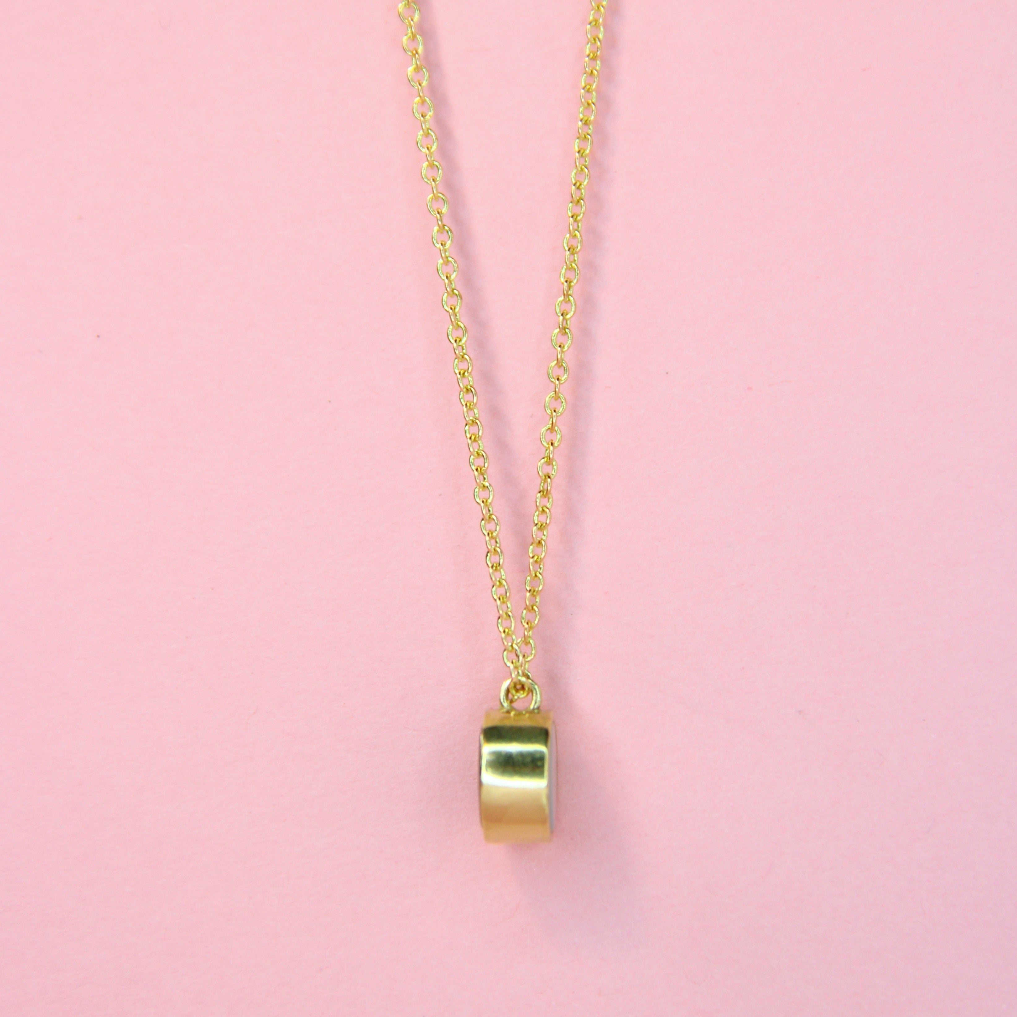 A side view of a gold toned bronze reversible charm necklace with a dainty chain 