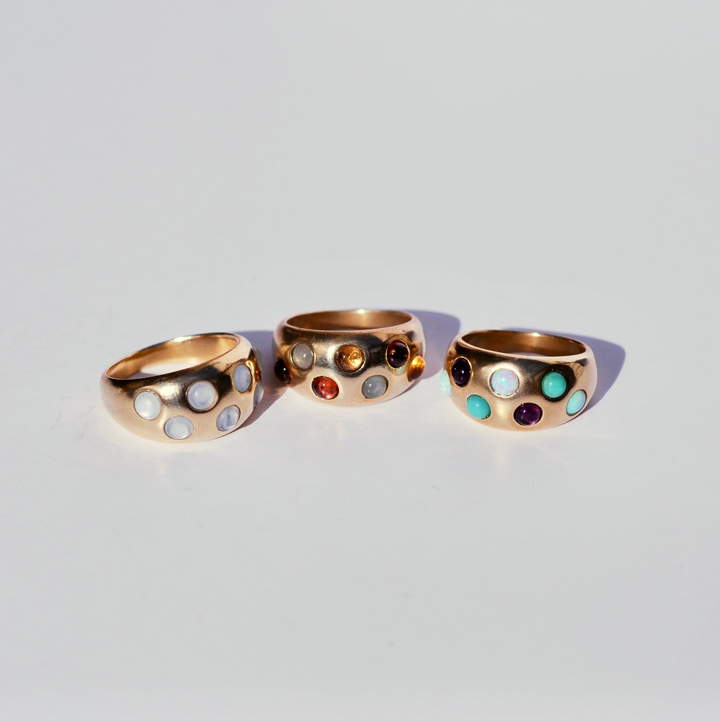 Three gold bronze rings with round cabochon gemstones in a polka dot pattern on a light gray background