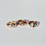 Three gold bronze rings with round cabochon gemstones in a polka dot pattern on a light gray background