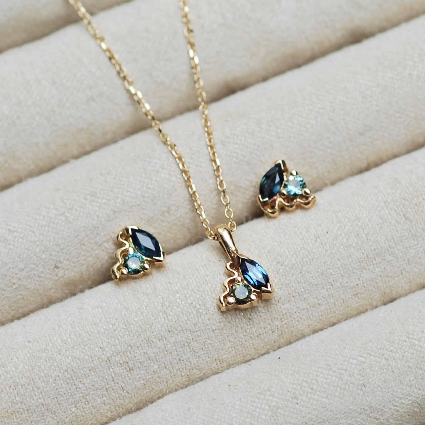 Gold necklace and earrings with blue sapphire gemstones on a beige surface