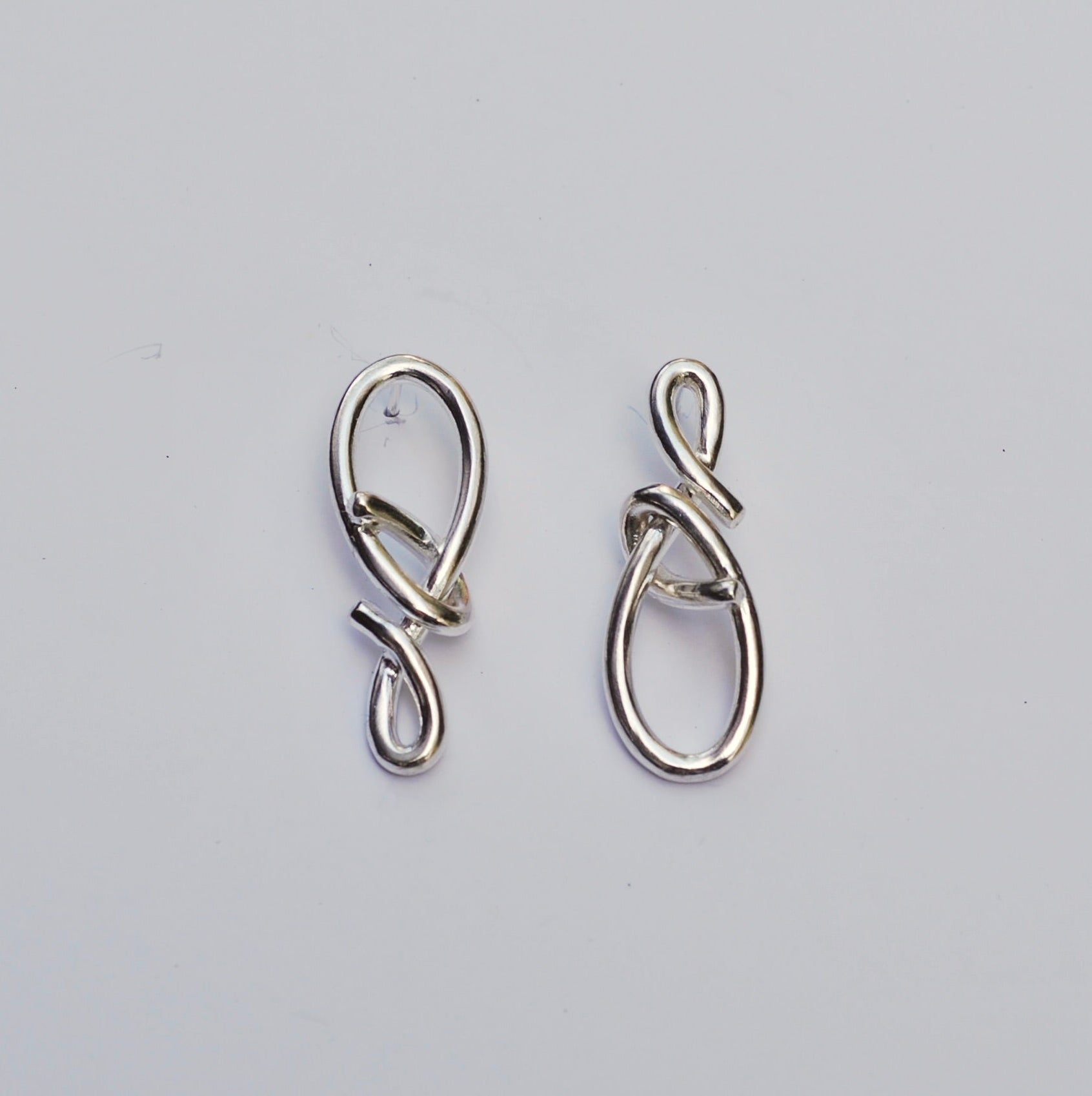Silver asymmetrical knot post earrings on a grey background