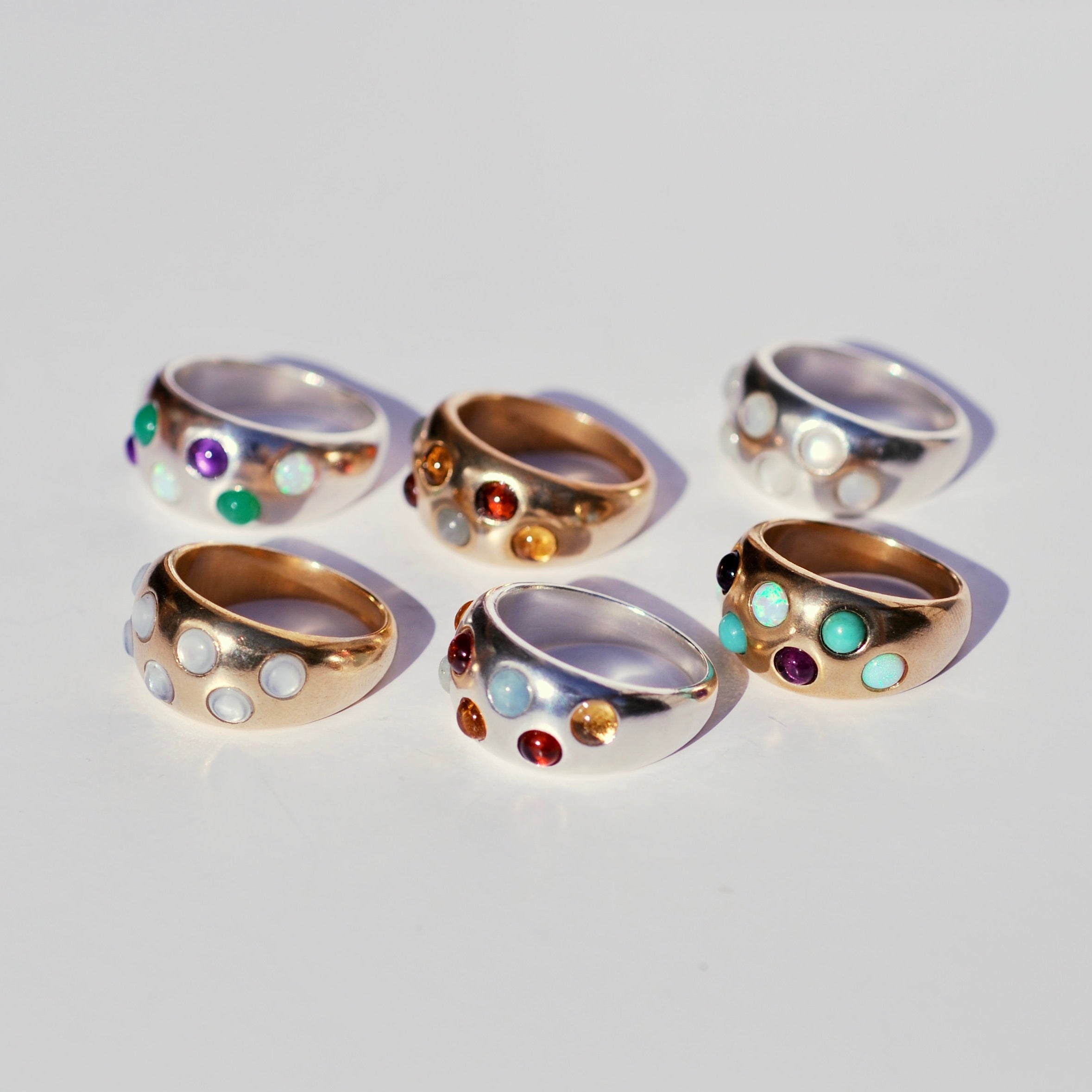 Set of six gold rings with round gemstones on a light gray background