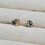 Pair of gold earrings with blue Australian sapphire gemstones on a beige fabric background