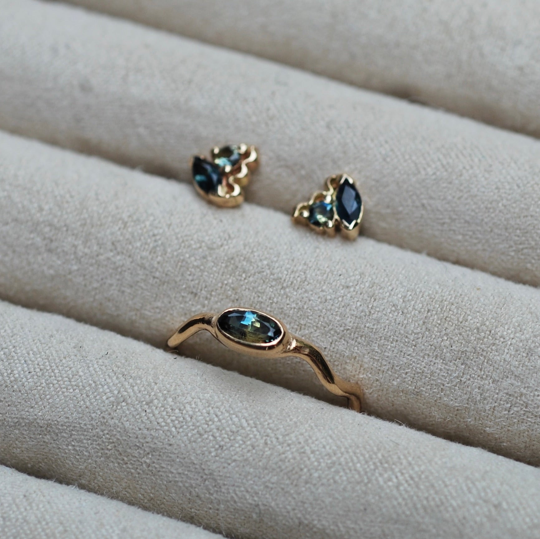 Gold ring and earrings with sapphire gemstones on a beige fabric surface