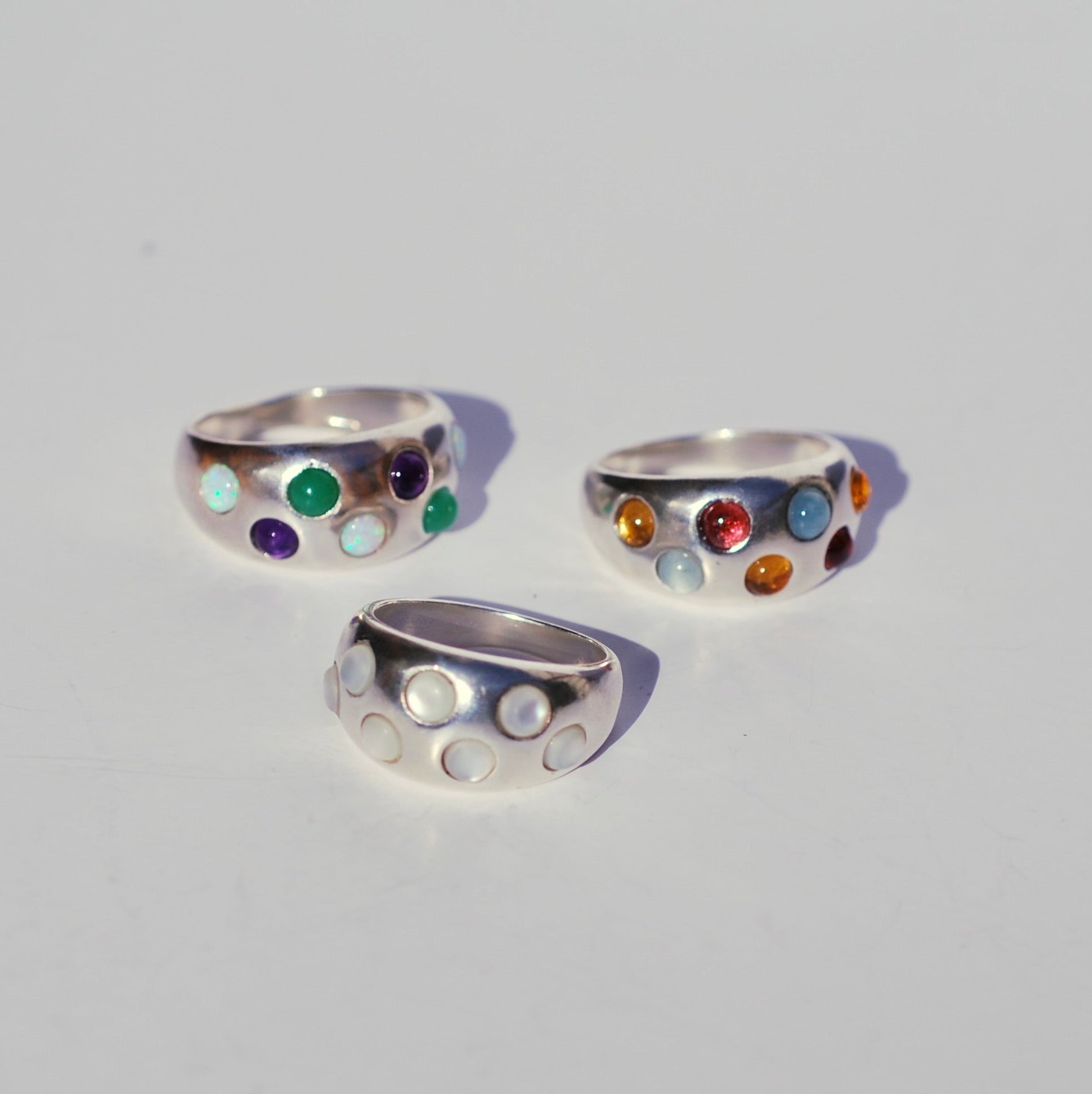 Three silver rings with colorful gemstones on a light gray background