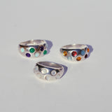 Three silver rings with colorful gemstones on a light gray background