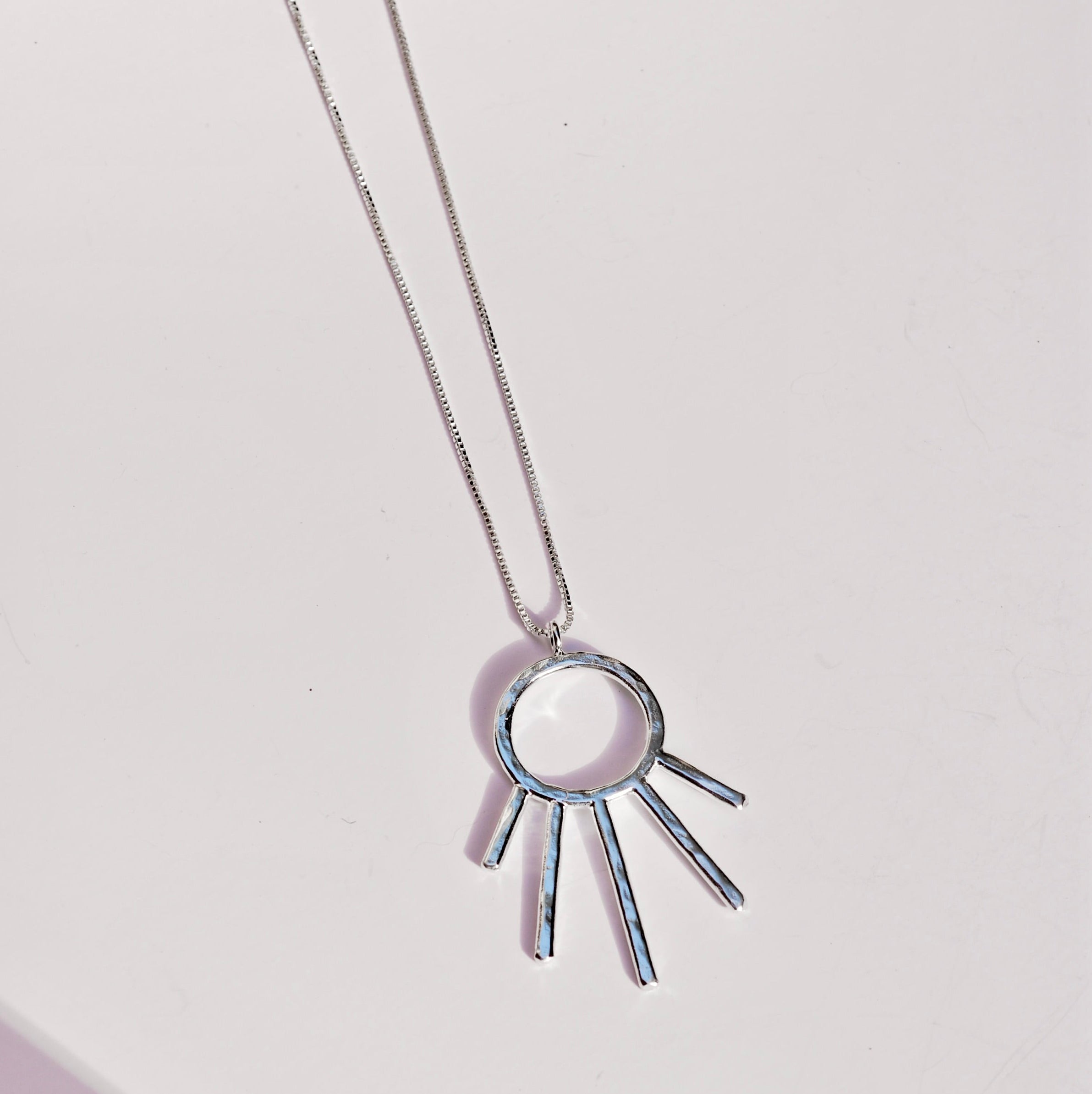 Silver necklace with a unique textured sunray pendant on a light gray background
