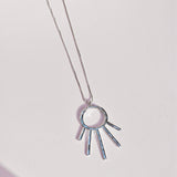 Silver necklace with a unique textured sunray pendant on a light gray background