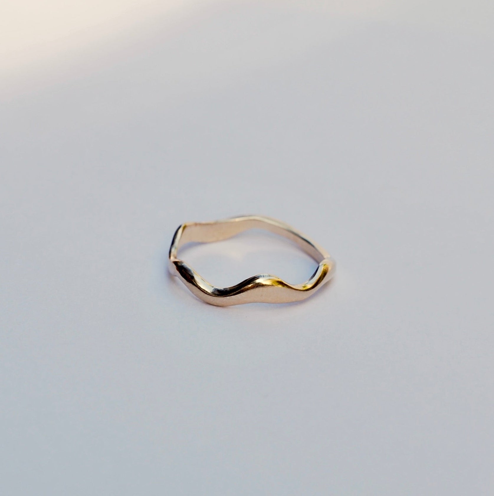 Gold ring with a wavy design on a light gray background