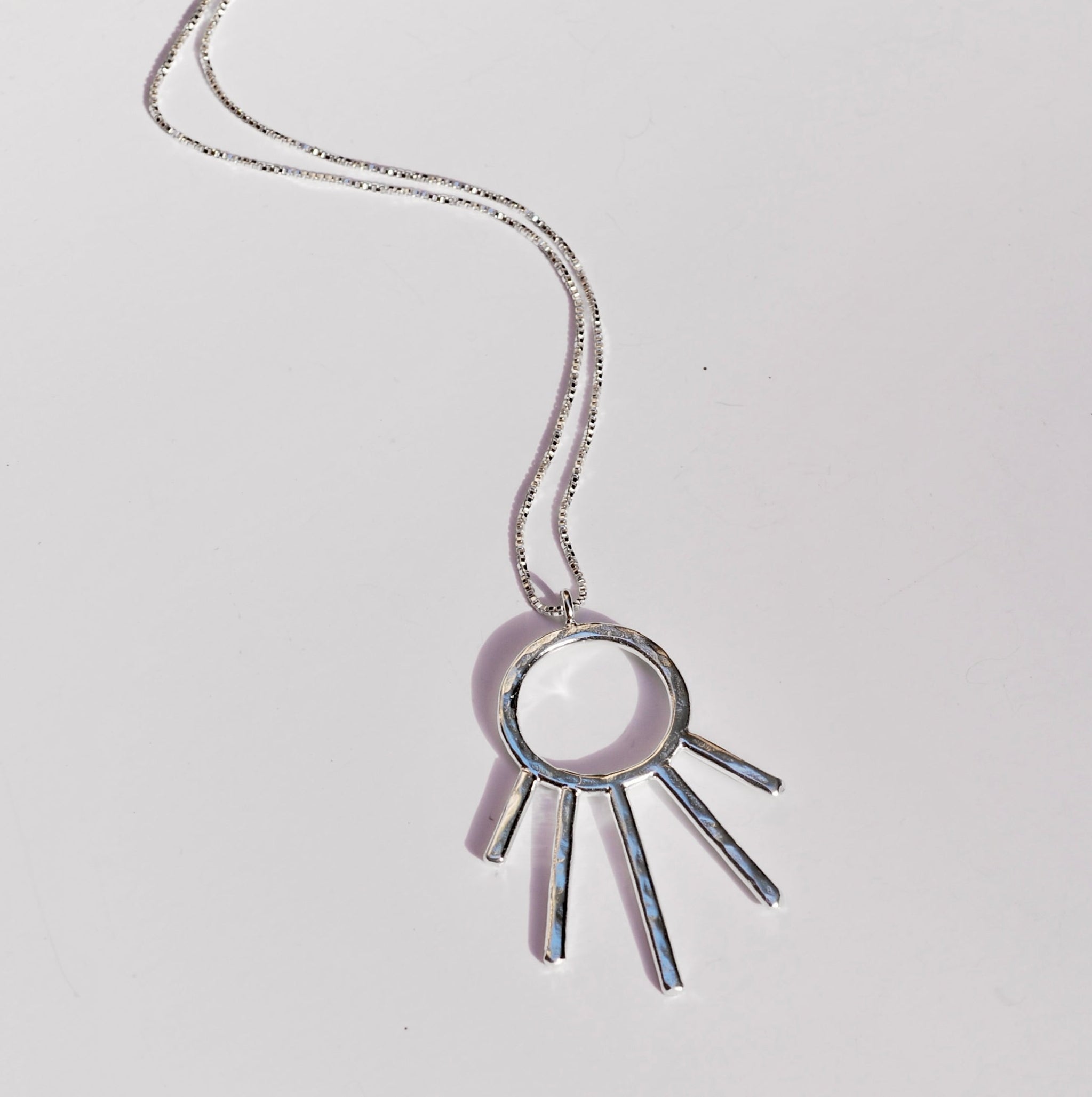 Silver necklace with a unique sunrise shaped pendant on a light gray background