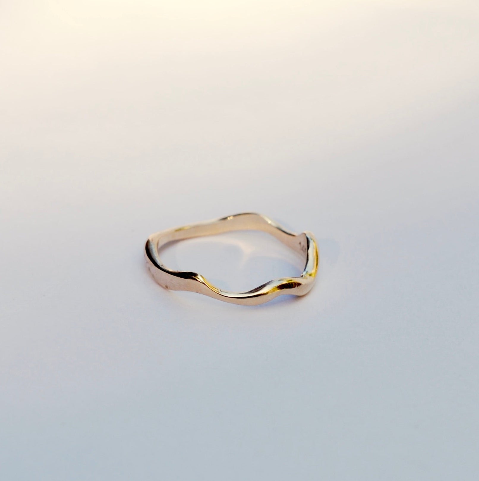 Gold ring with wavy design on a light gray background