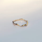 Gold ring with wavy design on a light gray background