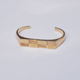 Bronze cuff bracelet with a checkerboard pattern in the metal sitting on a light grey background