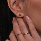 Close-up of an ear with a small earring with blue stones and a hand with rings on a blurred background