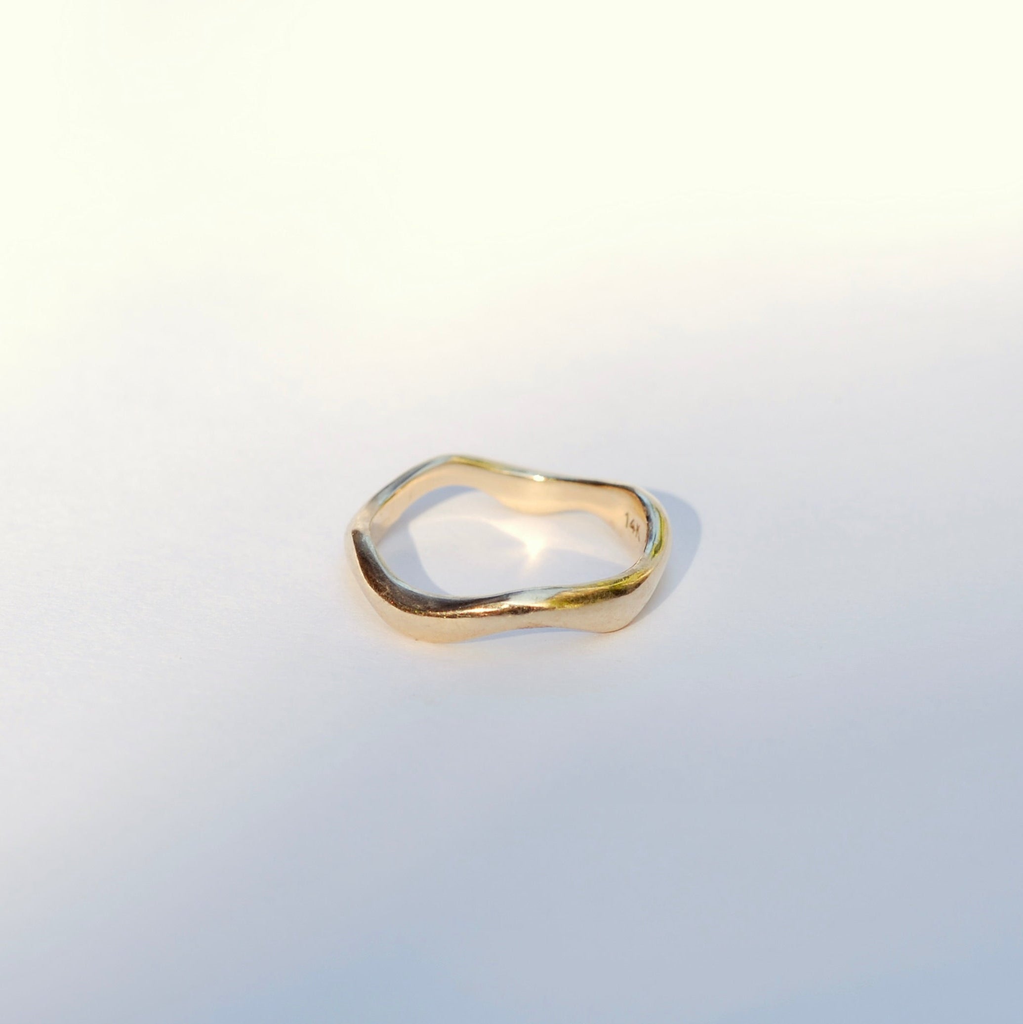 Gold organic wavy ring on a light gray background