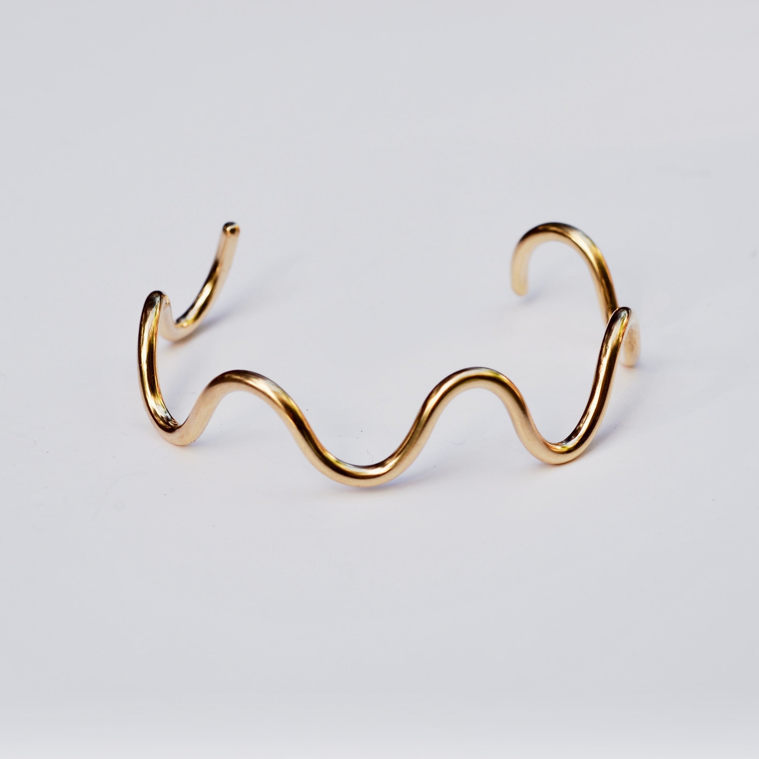 Gold wave-shaped bracelet on a light gray background