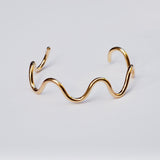 Gold wave-shaped bracelet on a light gray background