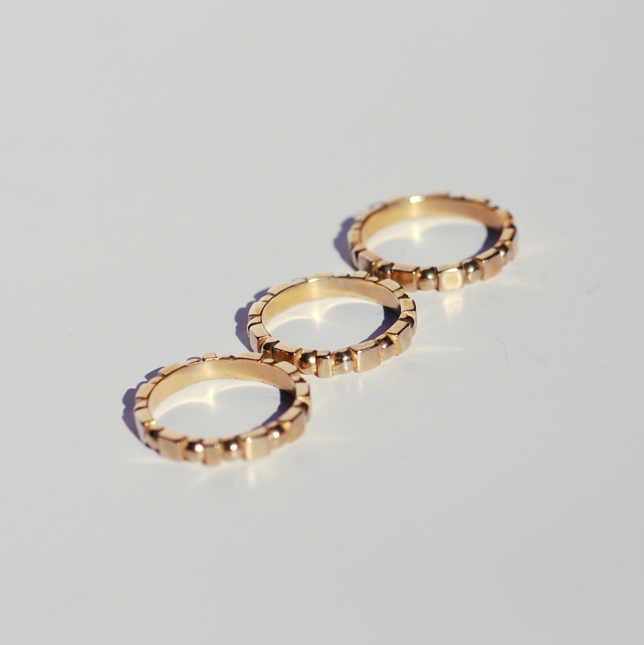 Three bronze ring bands with geometric patterns featuring squares and circles, sitting on a white background