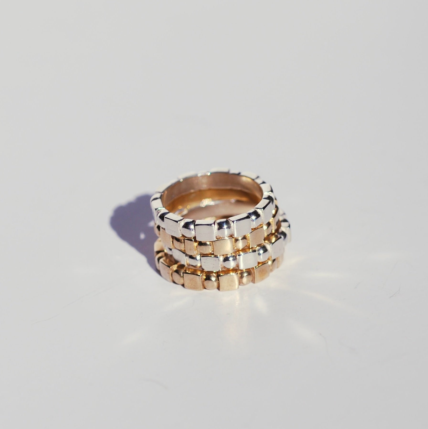 Four rings stacked on top of each other with square and round repeating geometric patterns 