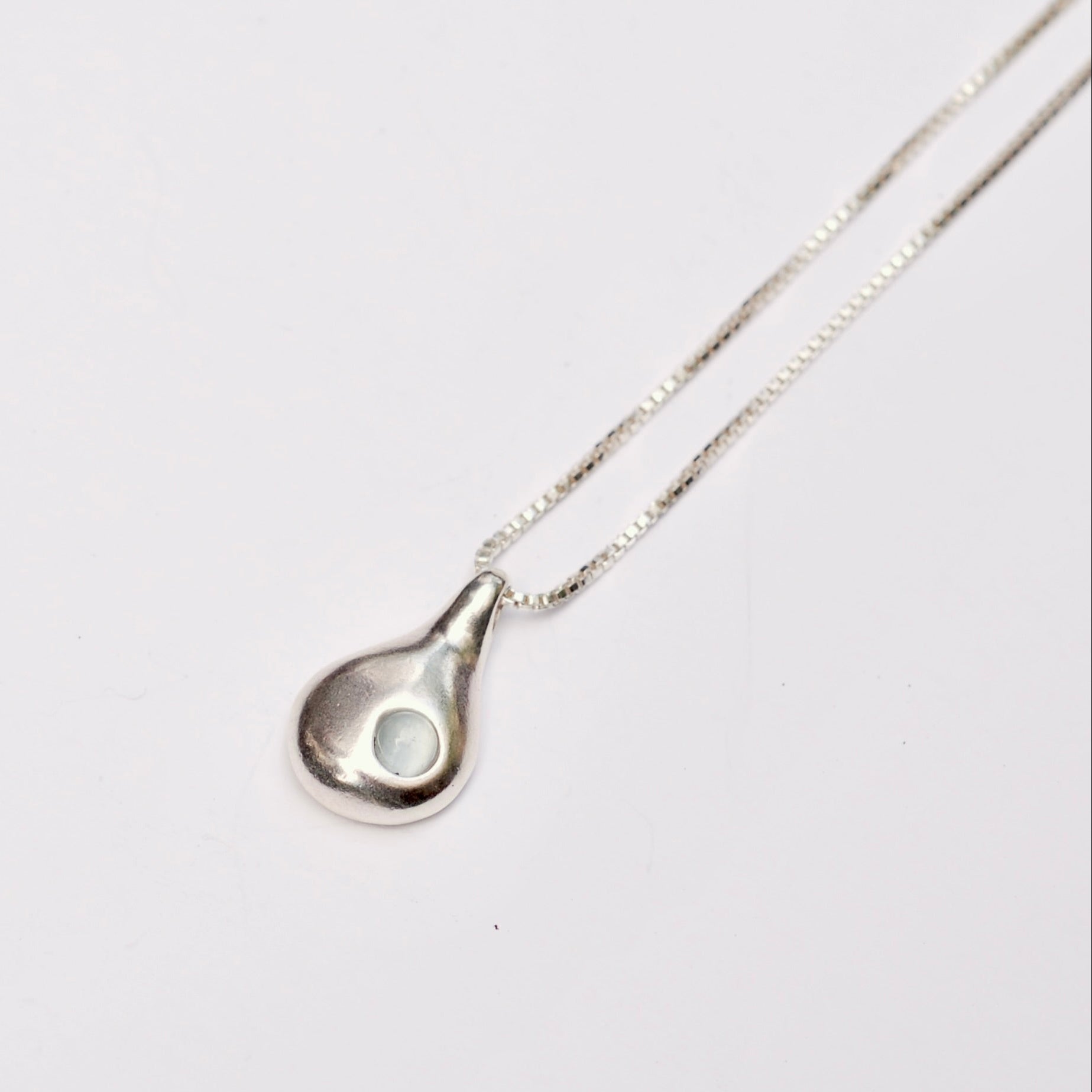 Silver teardrop pendant necklace with blue aquamarine stone on a white background