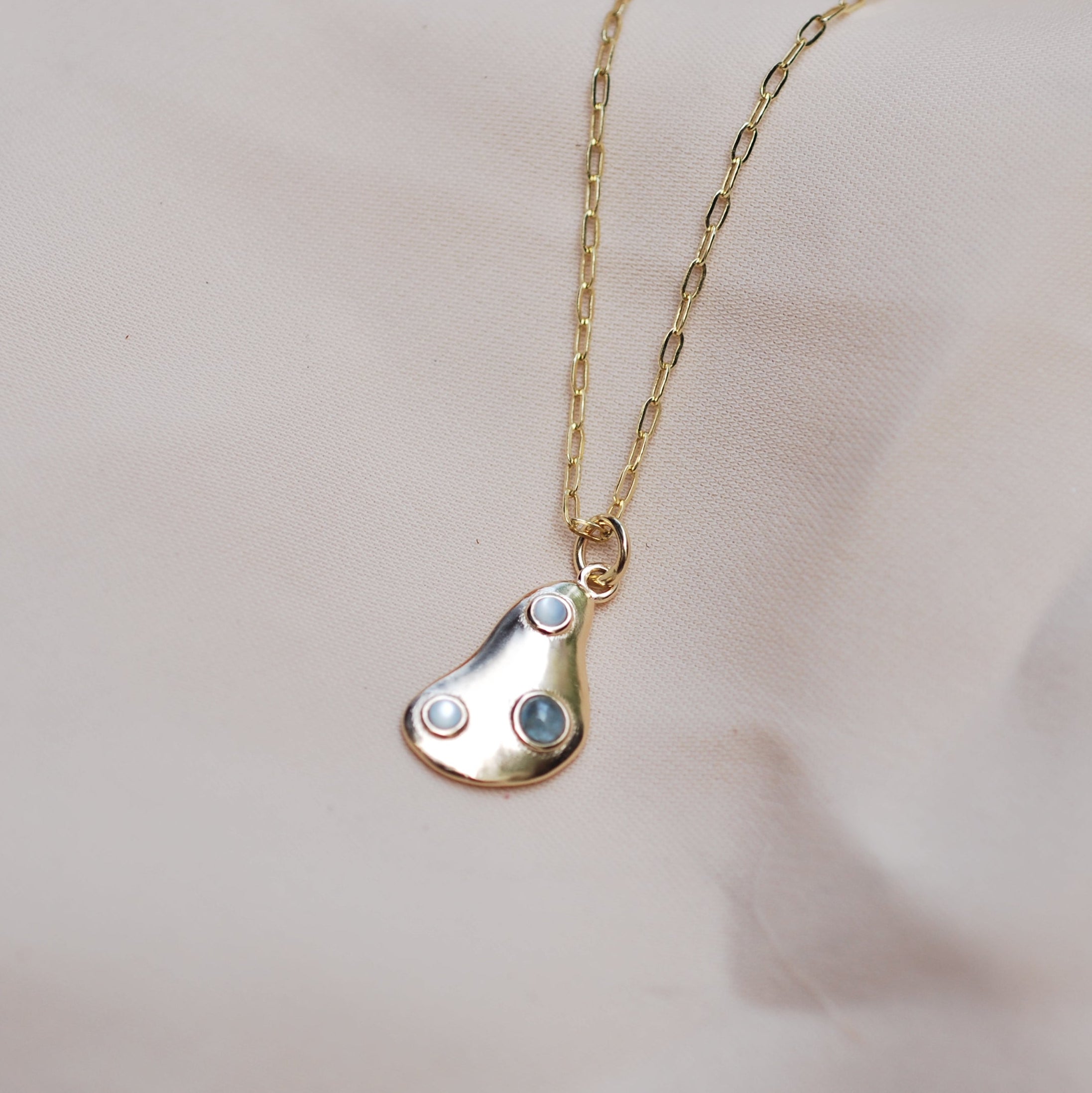 Gold necklace with a teardrop-shaped pendant and three cabochon stones on a light cream background
