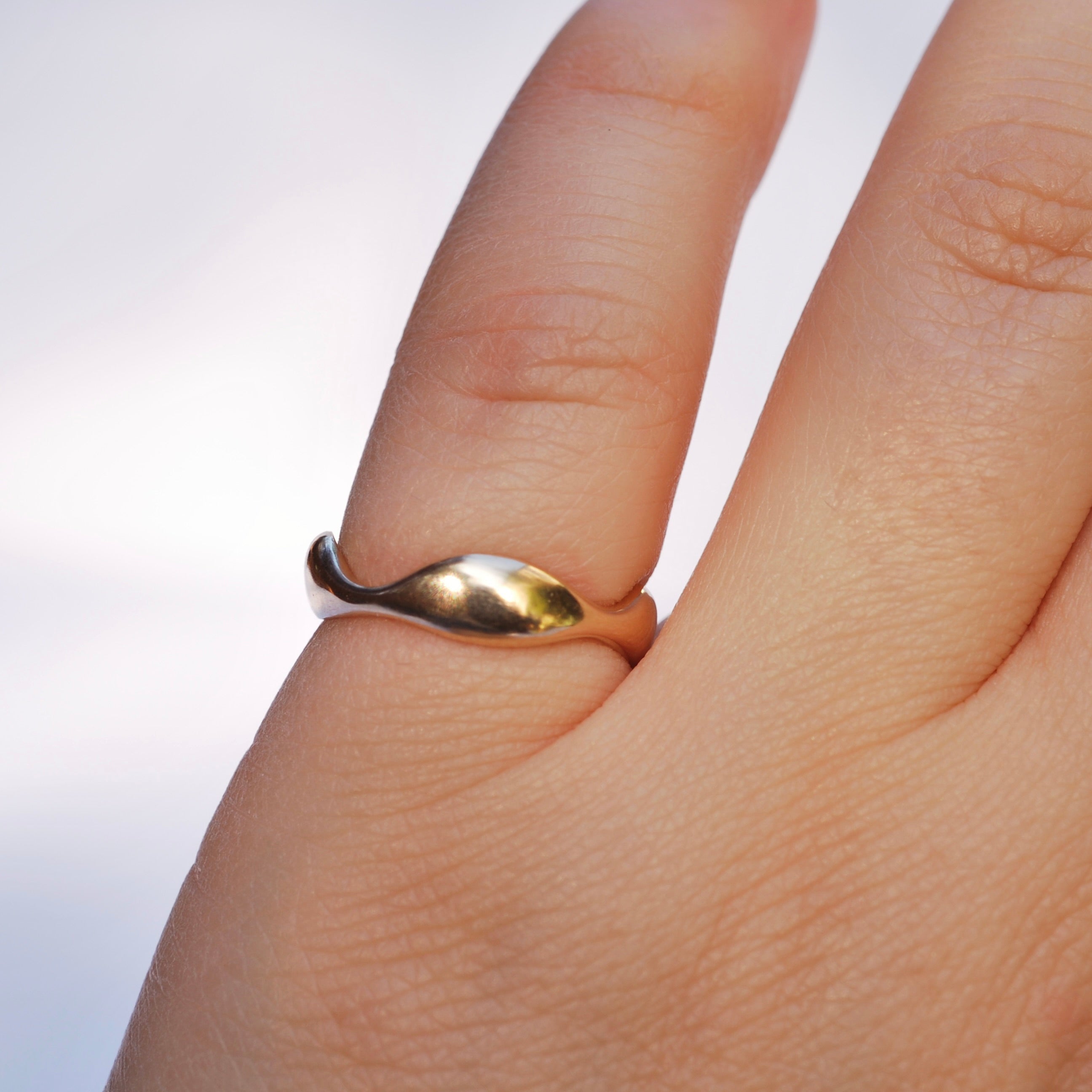 Gold wavy ring on a pinky with a white background