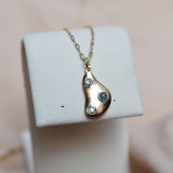 Gold necklace with a teardrop-shaped pendant on a white stand.