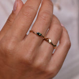 Close-up of a hand wearing a gold ring with a green gemstone on a blurred background
