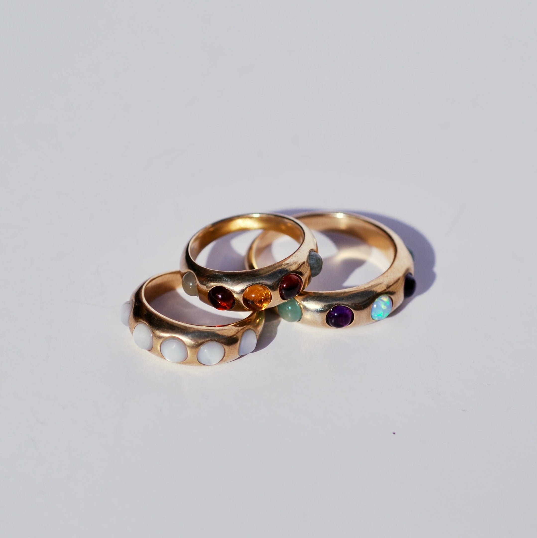 Three gold rings stacked on each other with embedded gemstones on a light gray background