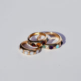 Three gold rings stacked on each other with embedded gemstones on a light gray background