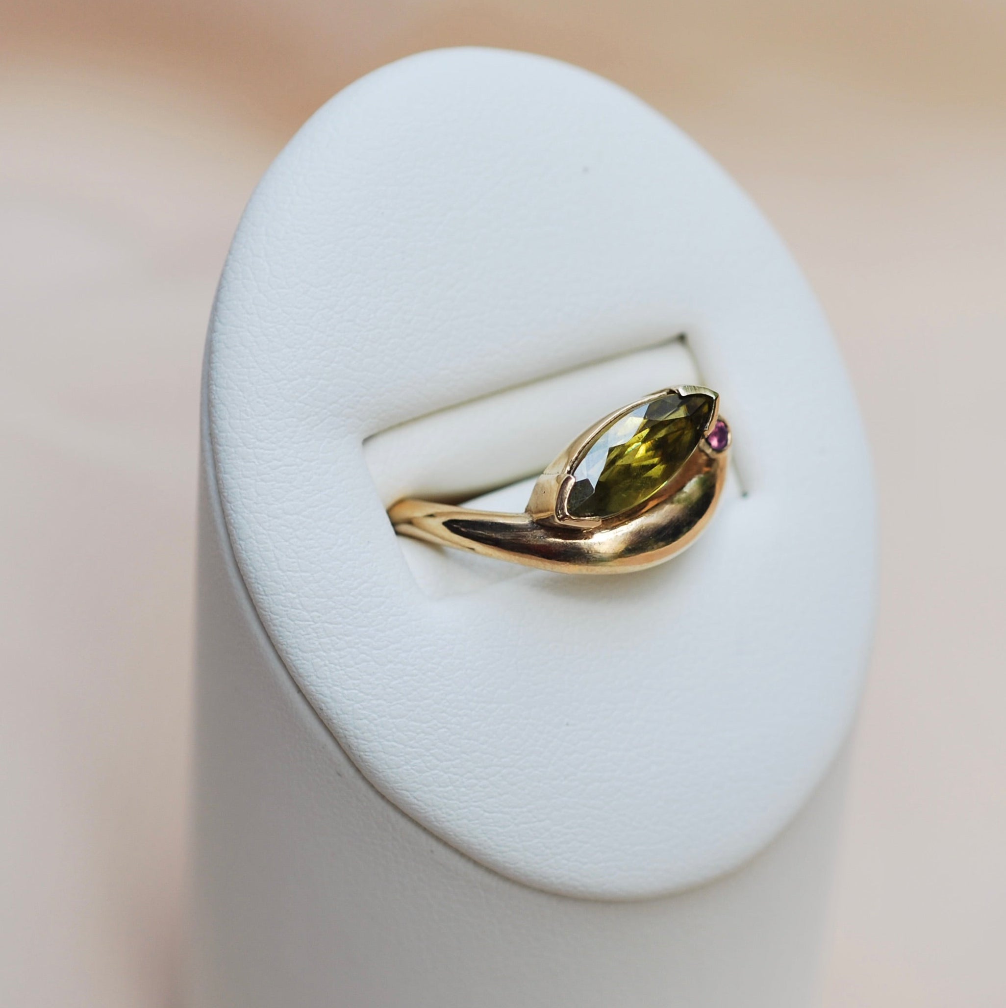 Side view of a ring with a swoopy gold band and a green marquis stone with a pink accent stone