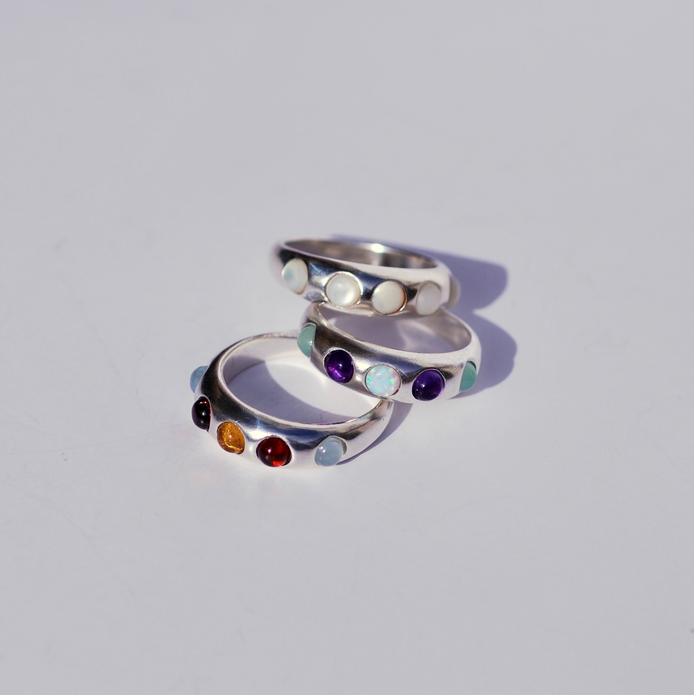 Three silver rings with colored gemstones on a light gray background