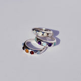 Three silver rings with colored gemstones on a light gray background