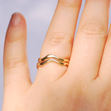 Two gold rings stacked together on a finger with a plain background