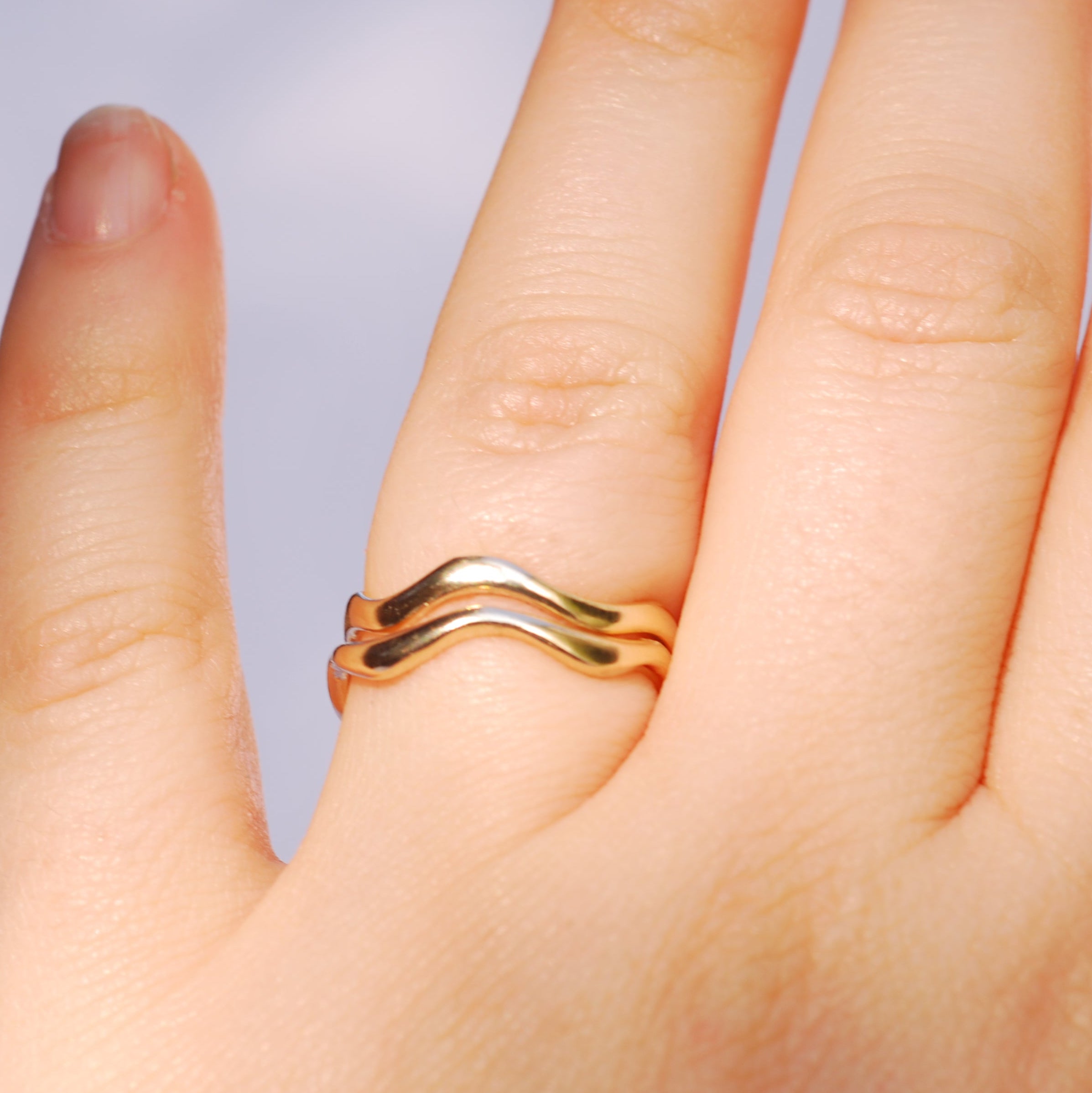 two gold rings stacked on a finger with a plain background