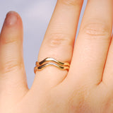 two gold rings stacked on a finger with a plain background
