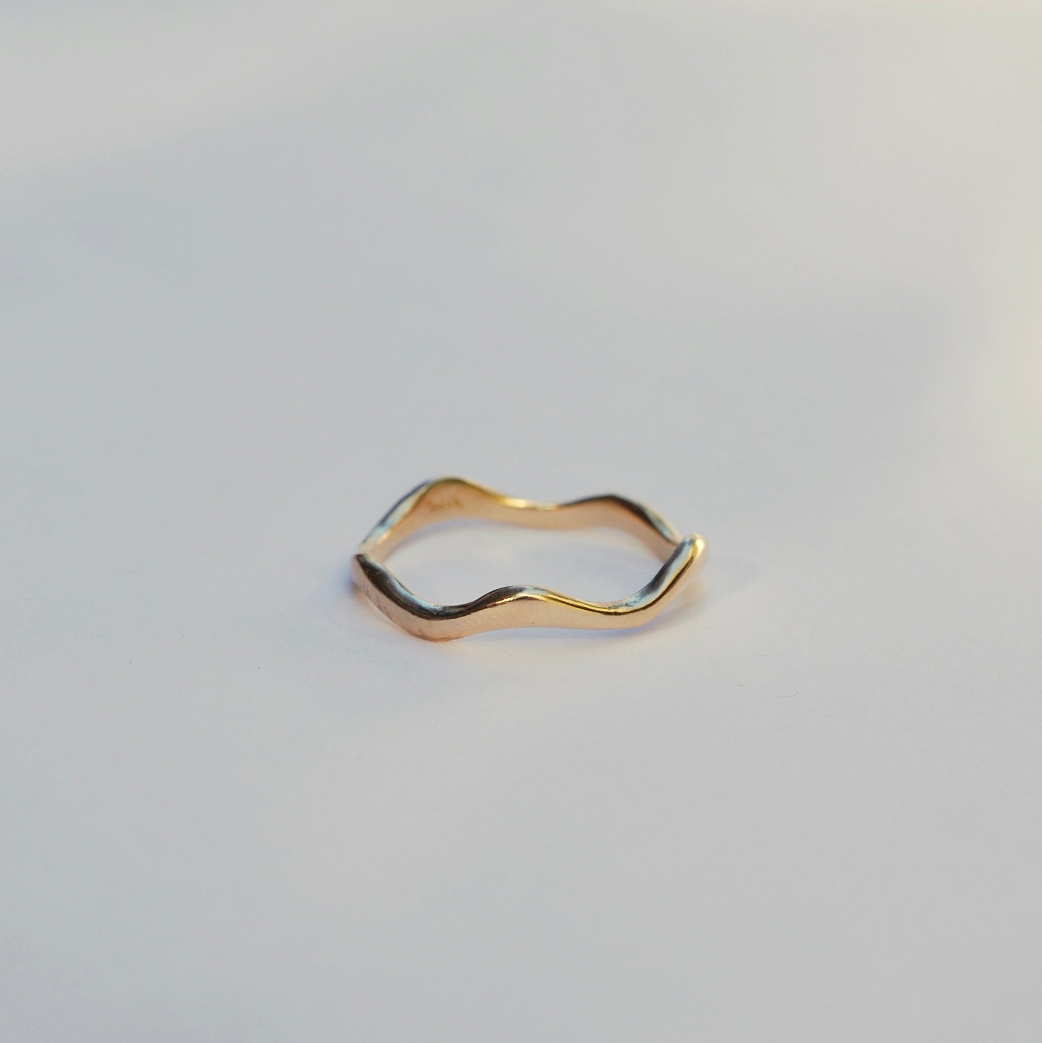 Gold ring with wavy design on a light gray background