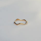 Gold ring with wavy design on a light gray background