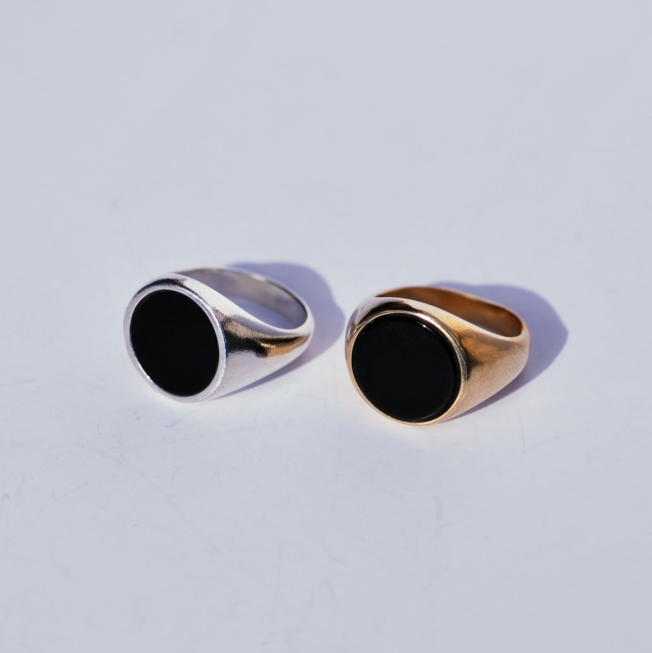 Two round signets with large black onyx inlay faces, one bronze and one silver on a white background