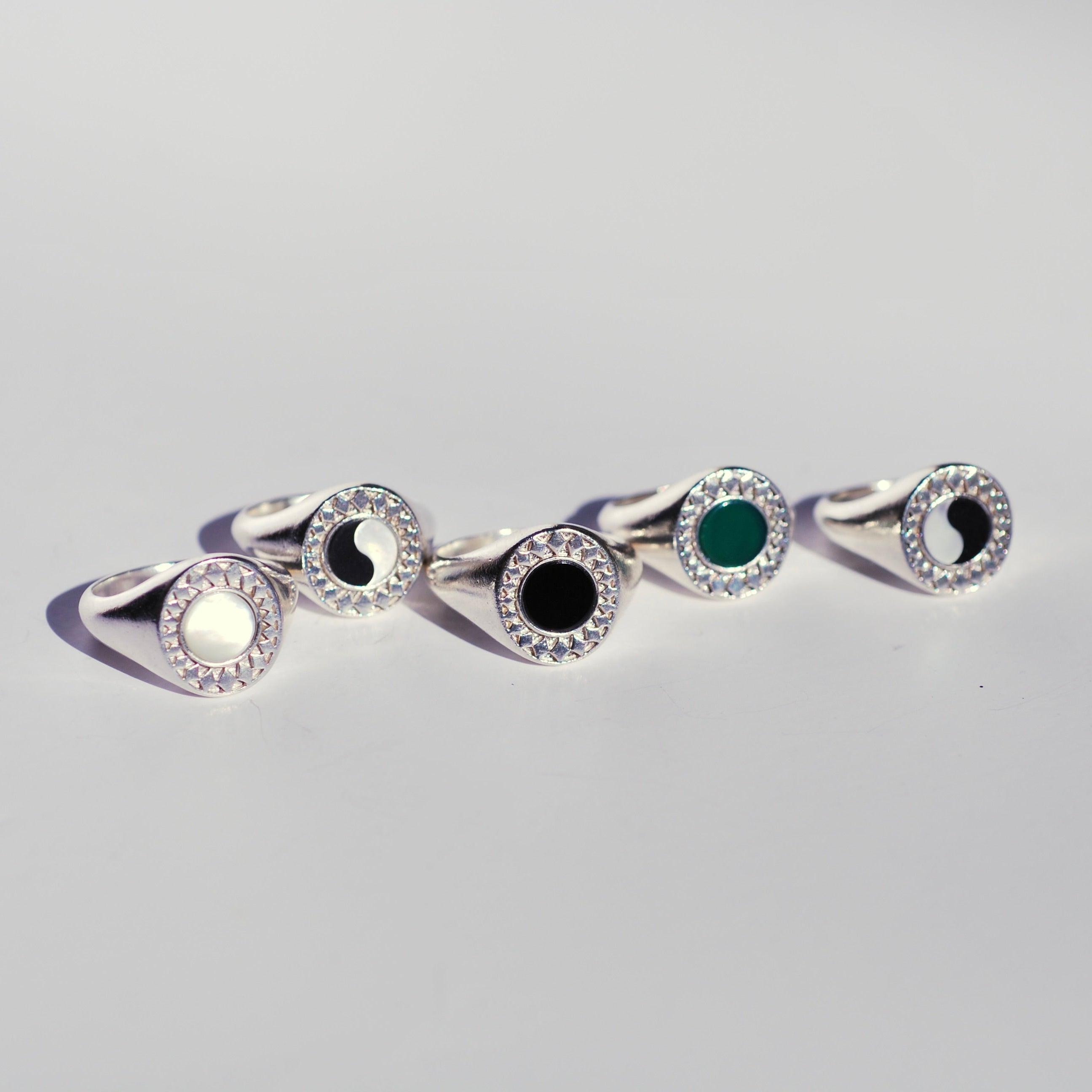 Five oval silver signet rings with different round center stones and a diamond burst pattern bordering the stones. 