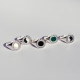 Five oval silver signet rings with different round center stones and a diamond burst pattern bordering the stones. 