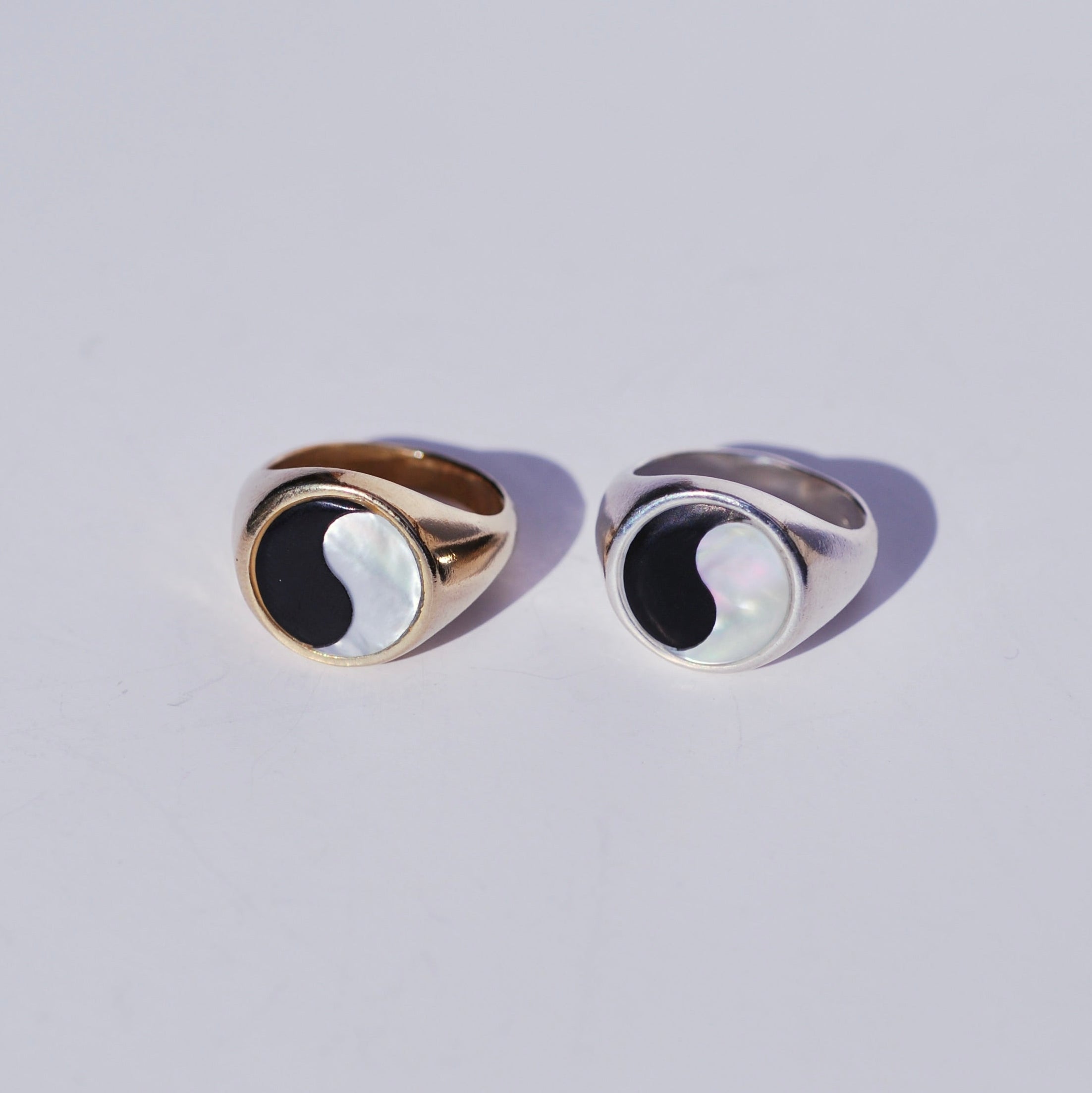 Two round signets with large ying yang inlay faces, one bronze and one silver on a white background