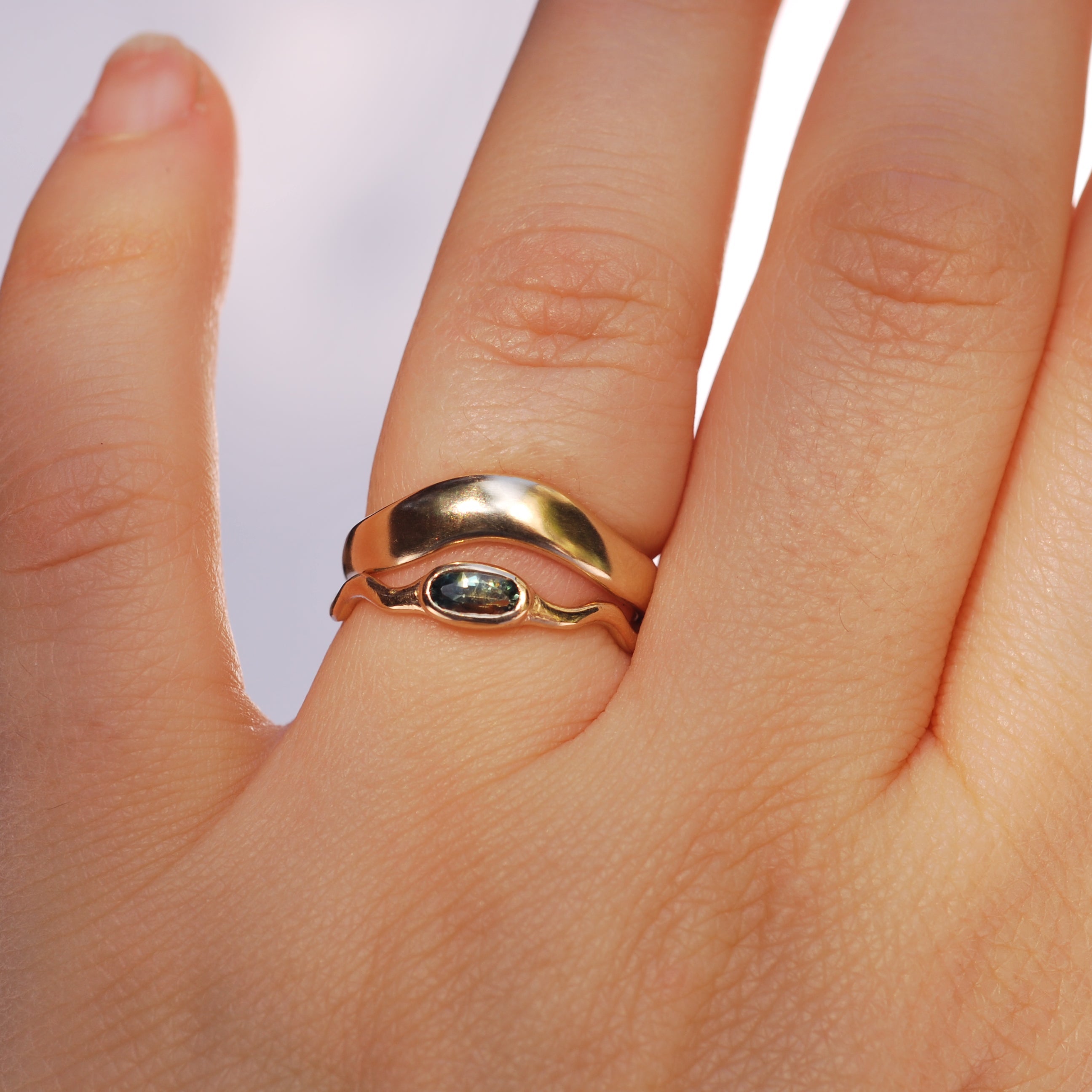 Gold ring stacked over a gold stone ring on a person's finger with a plain background