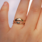 Gold ring stacked over a gold stone ring on a person's finger with a plain background