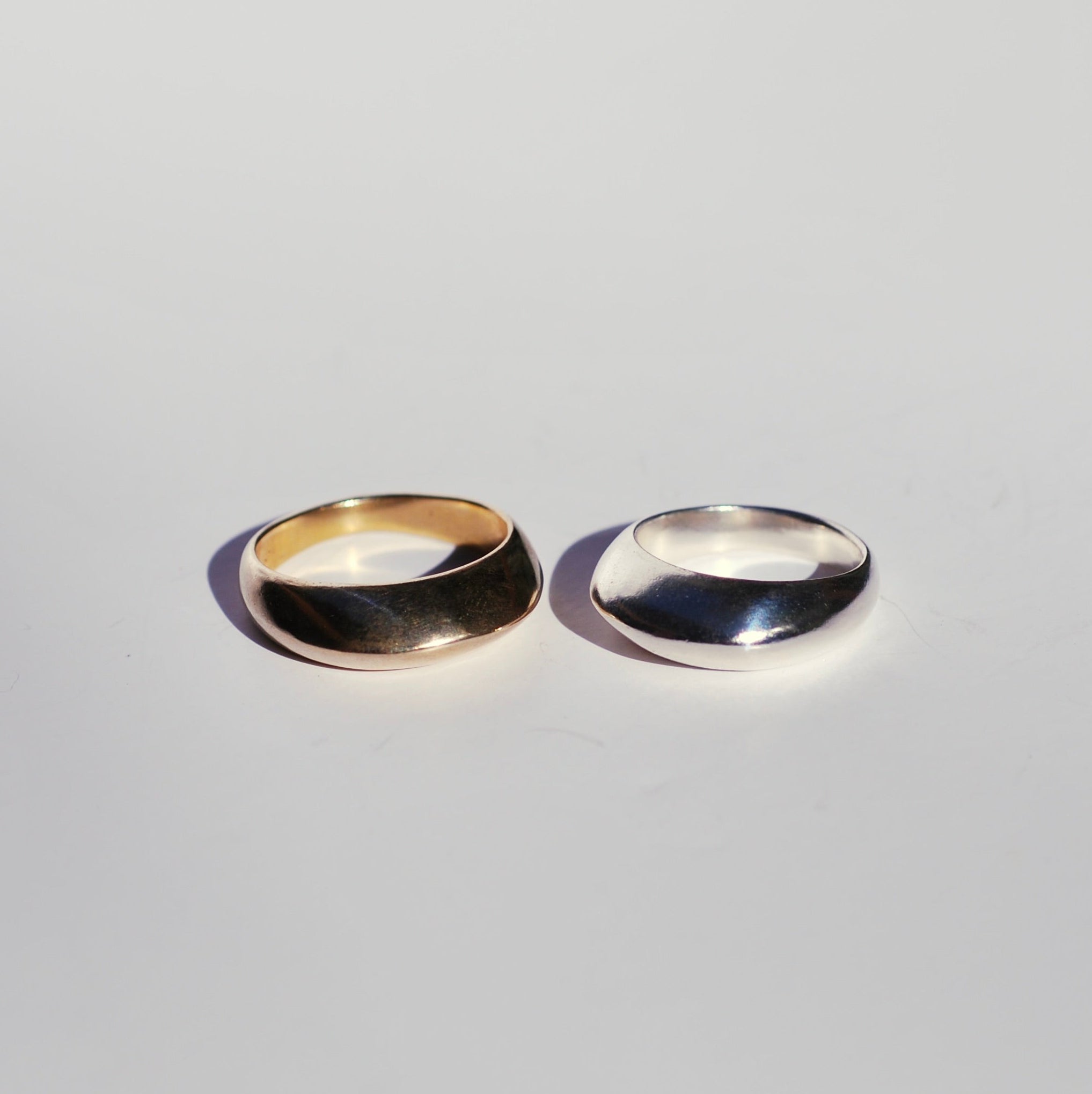 Front view of two rings, one bronze and one silver with a sculptural knife edge band